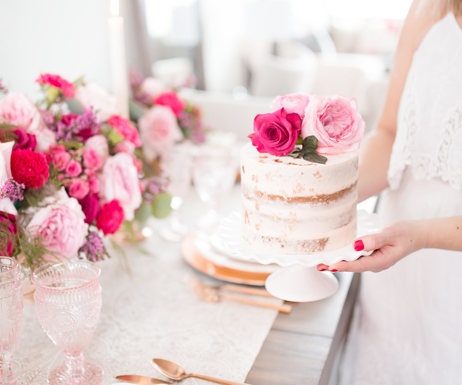 A beautifully crafted two-tiered cake with pink and fuchsia roses on a festive table setting, symbolizing the high-quality offerings of the bakery for sale.
